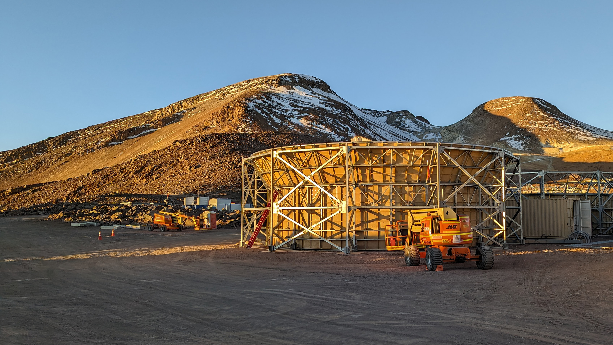 A telescope enclosure sits in front of two mountains under a blue sky