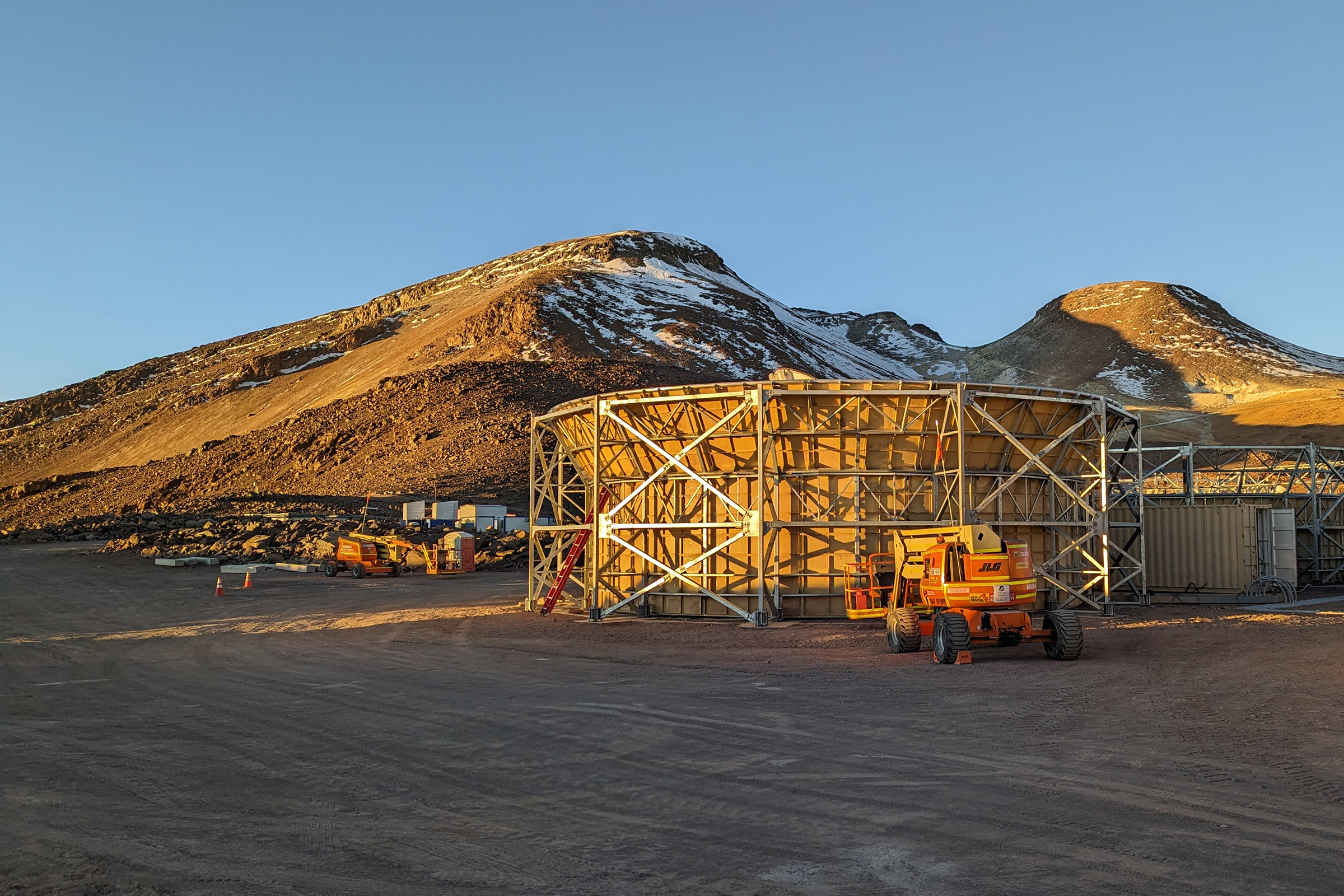 A telescope enclosure sits in front of two mountains under a blue sky