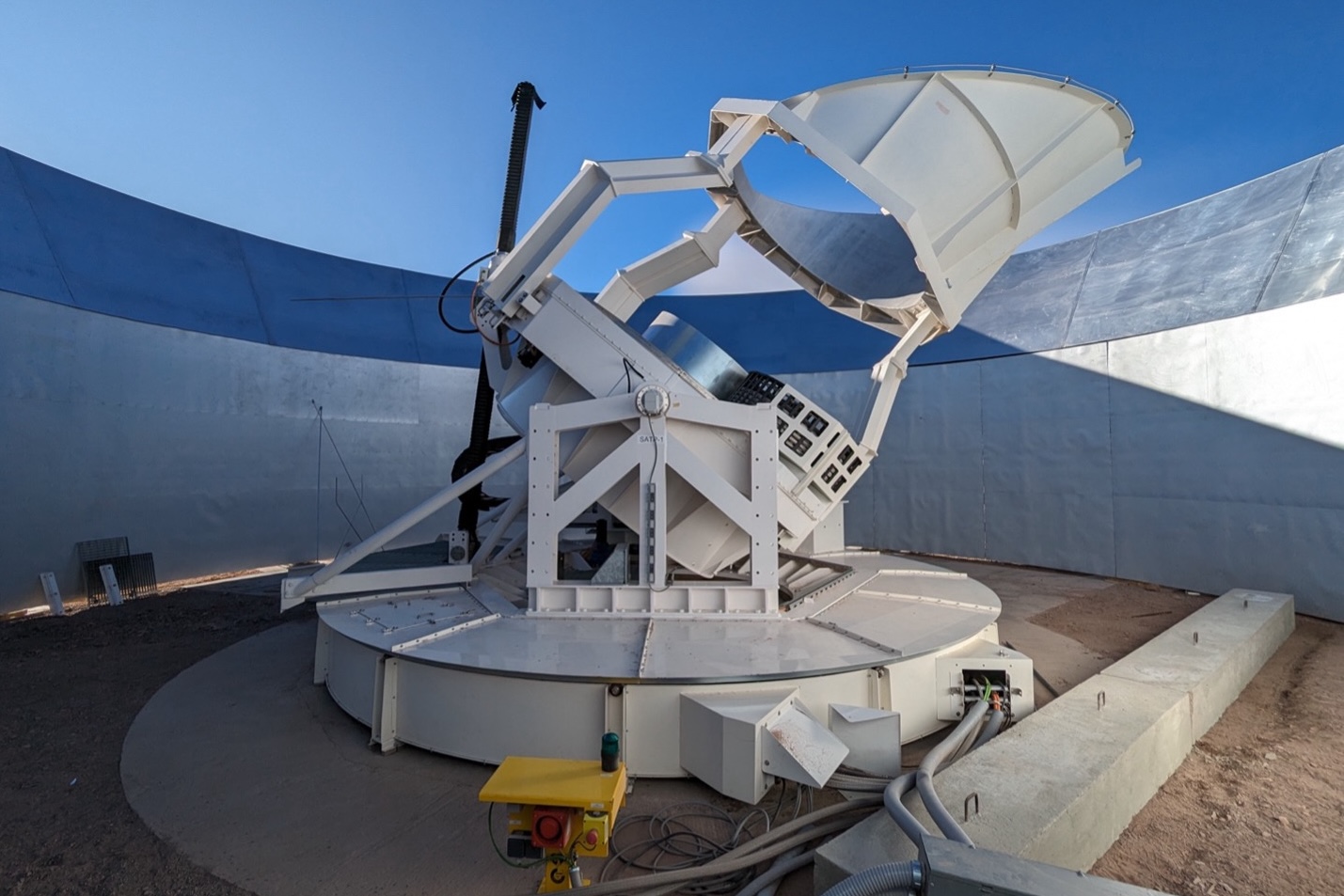 Under a blue sky on a rooftop a scientific instrument with cylinders like a telescope is plugged in and ready for operations